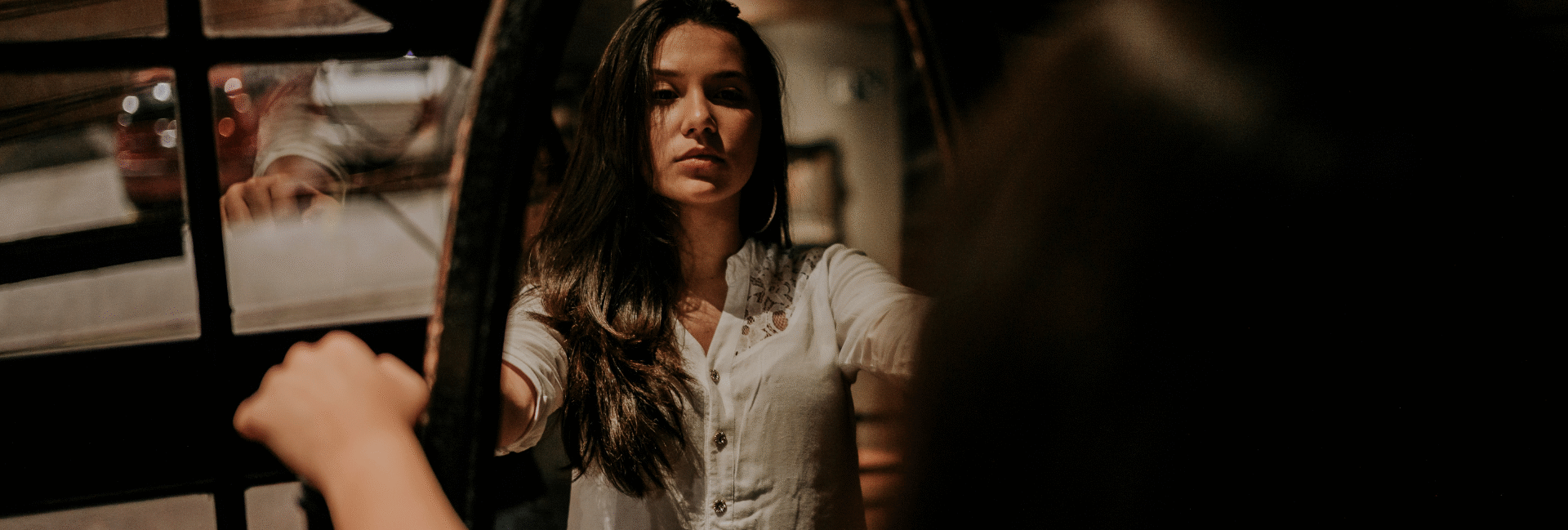 Mulher refletindo no espelho num ambiente à meia luz. A iaem representa o autoconhecimento e a autorregulação das próprias emoções que vêm com a inteligência emocional.
