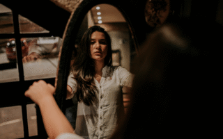 Mulher refletindo no espelho num ambiente à meia luz. A iaem representa o autoconhecimento e a autorregulação das próprias emoções que vêm com a inteligência emocional.