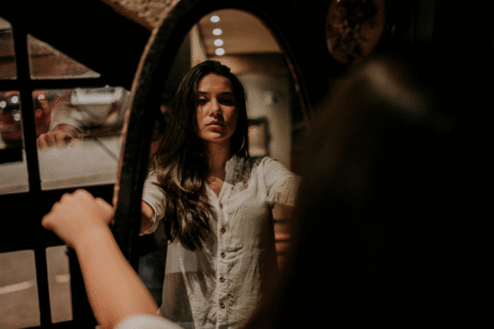 Mulher refletindo no espelho num ambiente à meia luz. A iaem representa o autoconhecimento e a autorregulação das próprias emoções que vêm com a inteligência emocional.